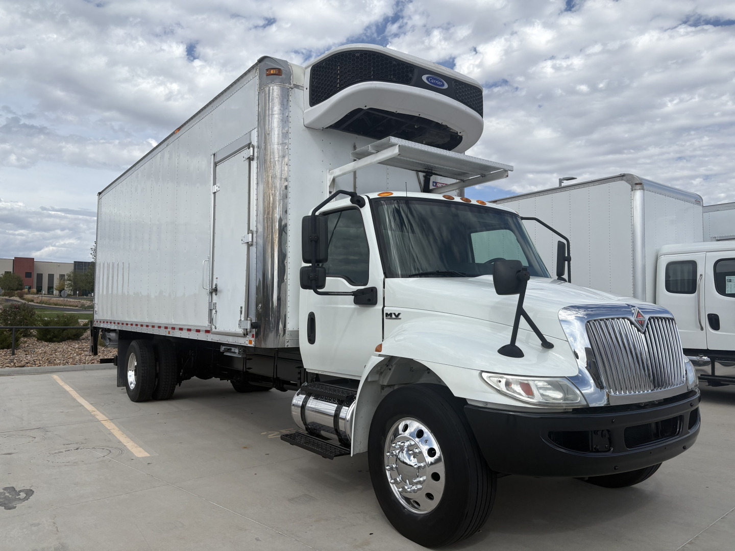 International MV607 refrigerated truck with a mounted cold storage refrigeration unit on a white cab and box, side view showing front grille and dual rear wheels.