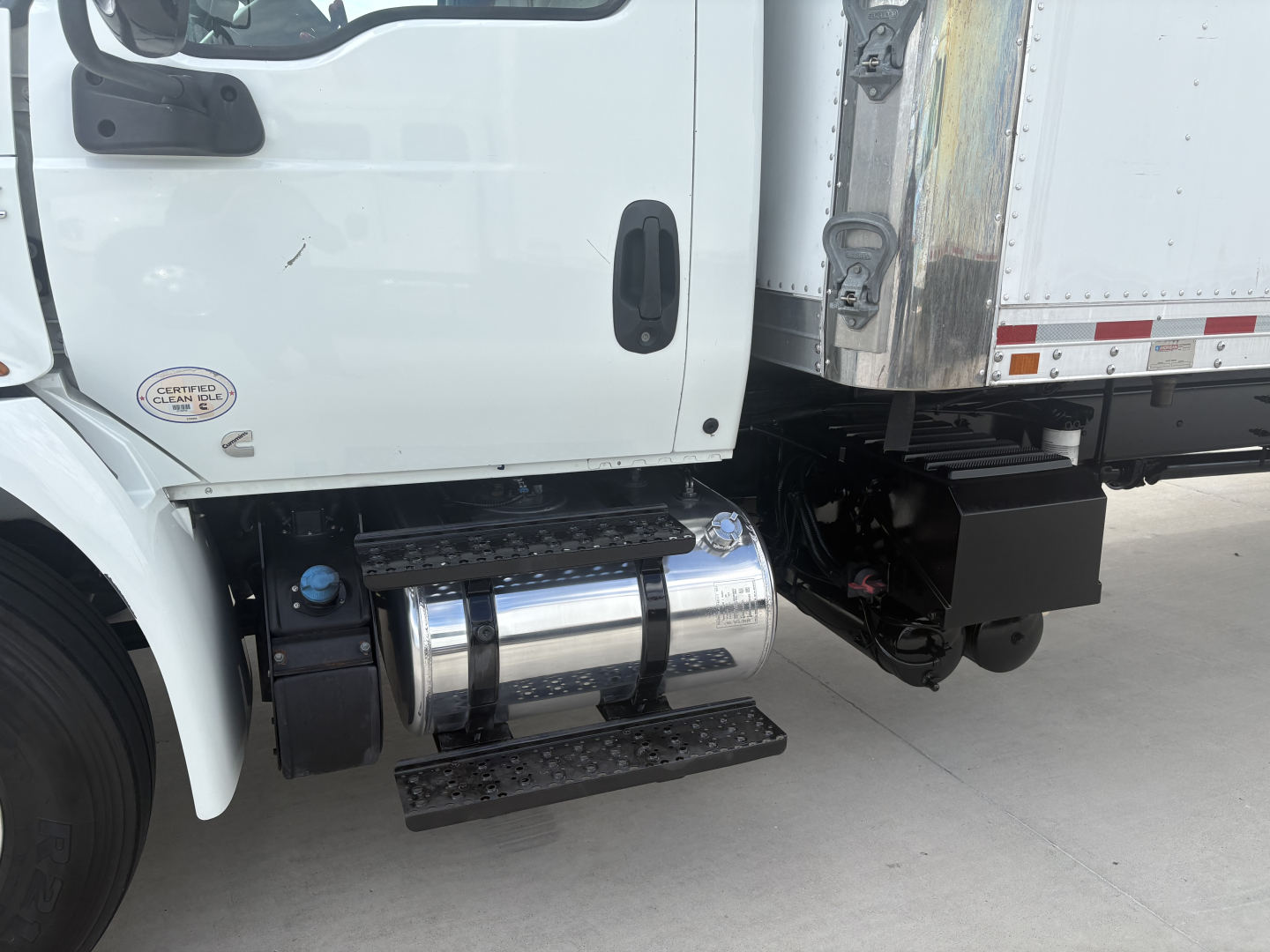 Trucking cab and side of refrigerated truck showing chrome aluminum fuel tank, step, and undercab components on the driver side of a 2021 International MV607.