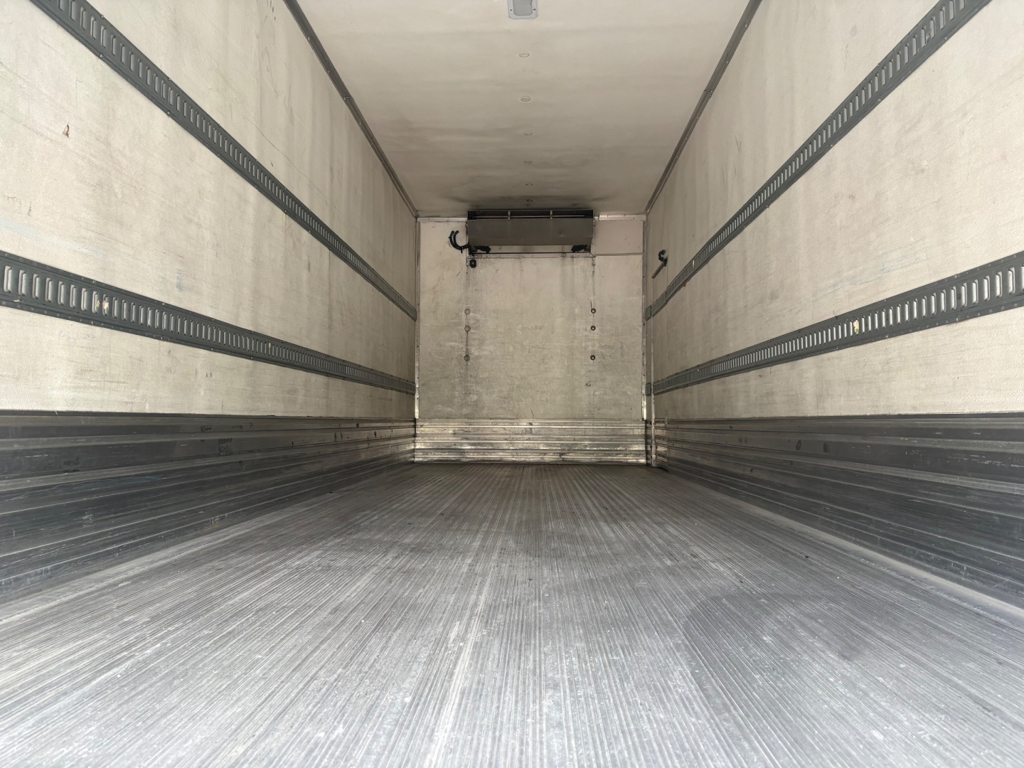 Inside view of a 2021 International MV607 refrigerated truck cargo area showing metal floor, side rails, and rear ceiling unit.