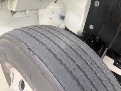 Front left wheel and fender of a 2021 International MV607 refrigerated truck showing tire tread and wheel well.