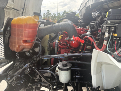 Truck engine bay showing coolant reservoir, red engine components, hoses, and white plastic air intake housing in a refrigerated 2021 International MV607.