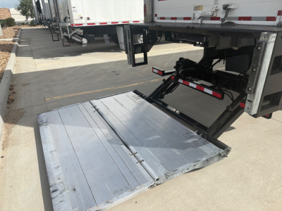 Truck liftgate deployed from a refrigerated International MV607 with a metal platform and hydraulic mechanism visible.