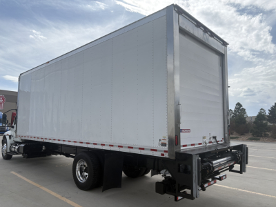 Truck trailer side and rear showing a white refrigerated box on a dual rear axle with a roll-up rear door and black undercarriage.