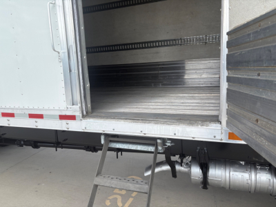 Truck refrigerated trailer interior with metal flooring and side rails; bottom step ladder at cargo door; cylindrical fuel or air tank and drive line visible