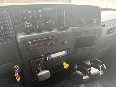 Dashboard view of a 2021 International MV607 truck interior showing HVAC controls, stereo, ignition with yellow key tag, and cup holders.
