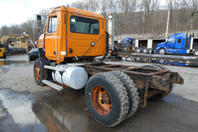 Truck cab and chassis of a 1998 Mack CH612 with orange cab, dual rear tires, and plow equipment in yard.