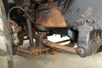 Mack CH612 truck chassis area showing front suspension components, leaf spring, and rusty frame with plow-related hardware.