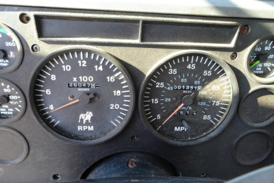 Instrumentation panel of a Mack CH612 truck showing two round gauges: left tachometer labeled RPM x100 with numbers and an odometer beneath; right speedometer labeled MPH with numbers and a mileage reading. Various other small gauges at edg