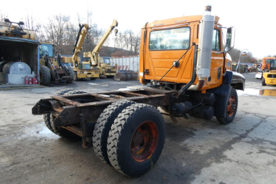 Truck chassis and orange Mack CH612 cab in-yard showing bare frame and dual rear wheels.