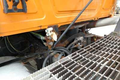 Mack CH612 truck undercarriage showing hydraulic lines and step grating near the cab; orange body panels and mounting hardware visible.