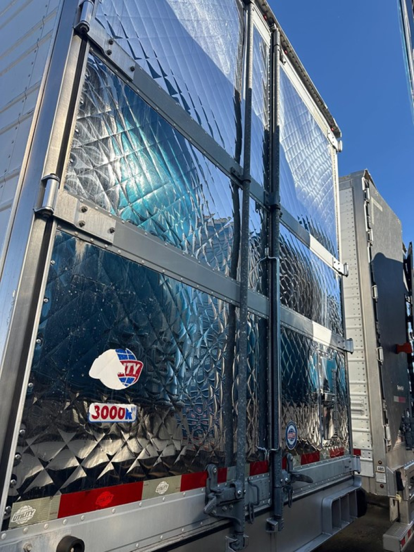 Trailer rear showing reflective aluminum doors with diamond plate pattern and latching hardware; Utility 3000R logo sticker visible on door.