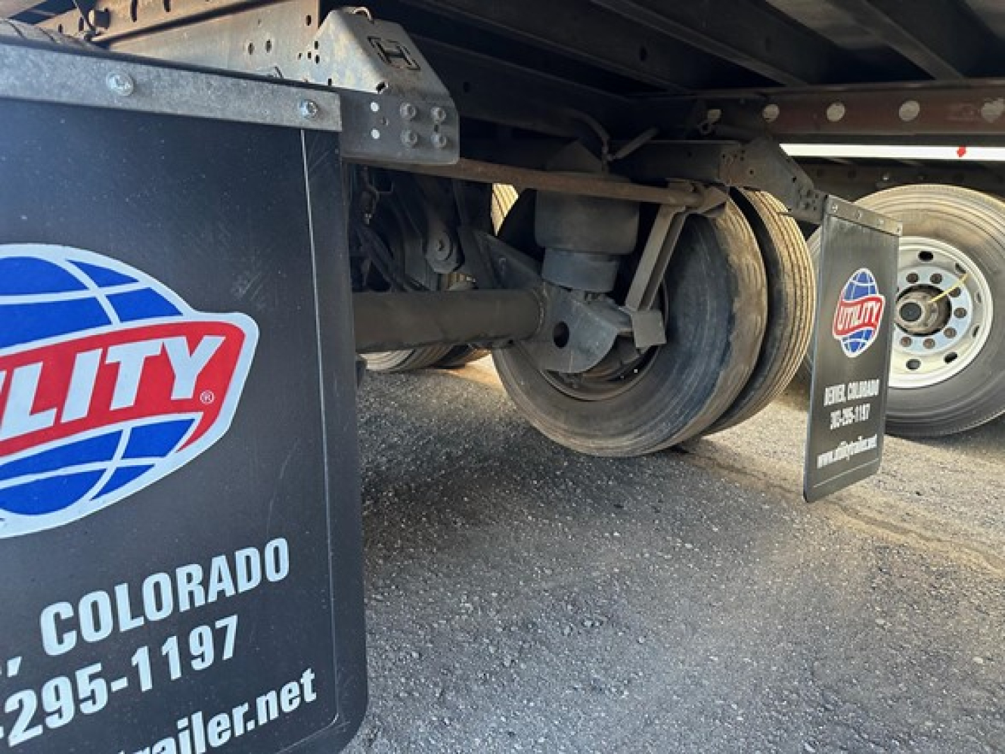 Trailer undercarriage with wheel and suspension visible; Utility logo mudflap and parts label visible.