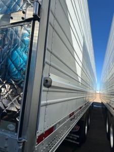 Trailer side view of a Utility 3000R refrigerated trailer showing metal cladding, hinge hardware, and a portion of the dual-axle setup.