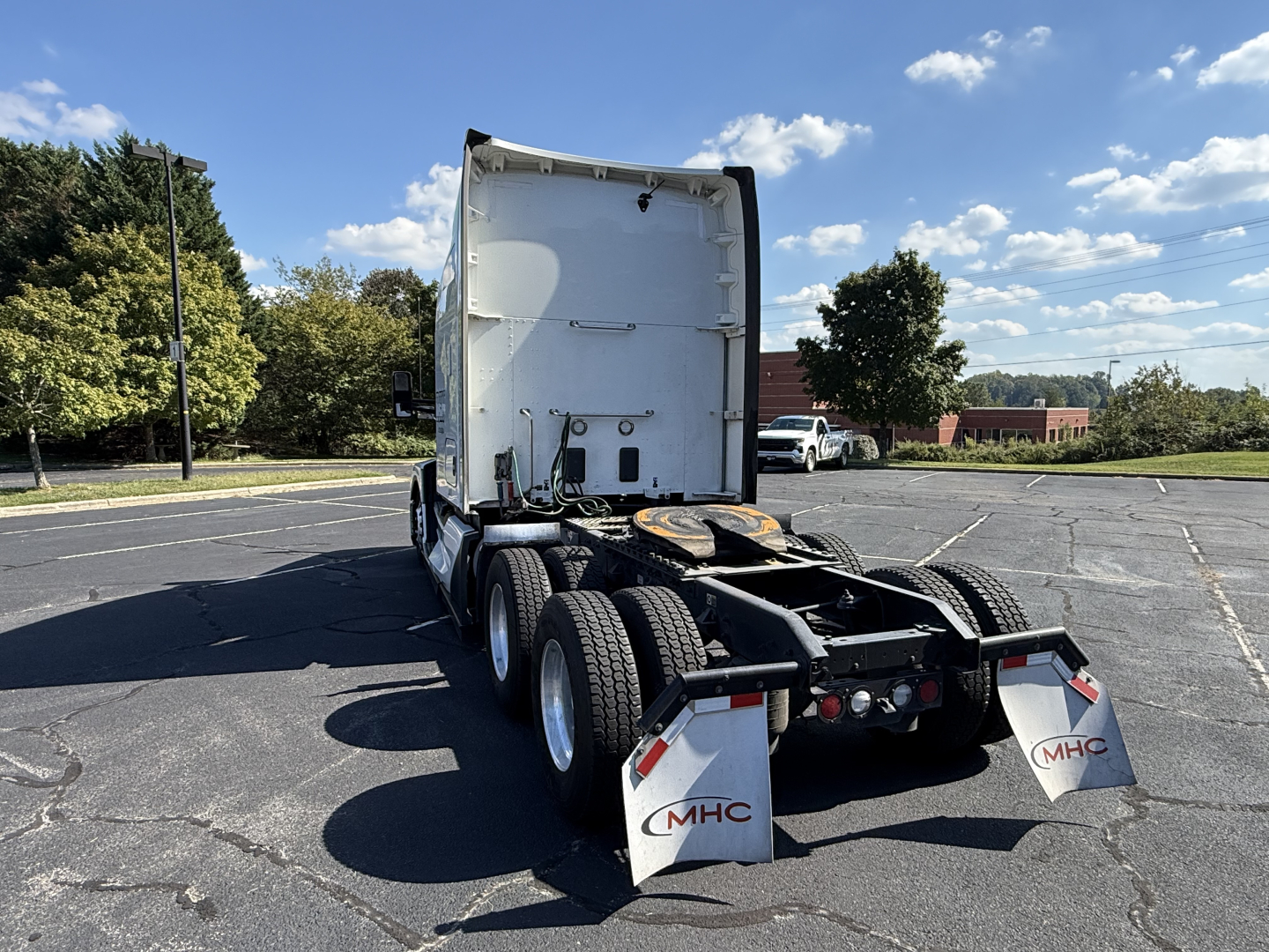 Kenworth T680 tractor rear view showing fifth-wheel plate, dual rear axles, mudflaps with MHC logo, and white sleeper cab.