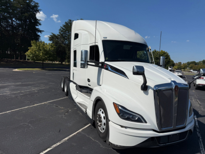 Kenworth T680 tractor in a parking lot, white cab with black grille, side mirrors, and sleeper, front view angled.