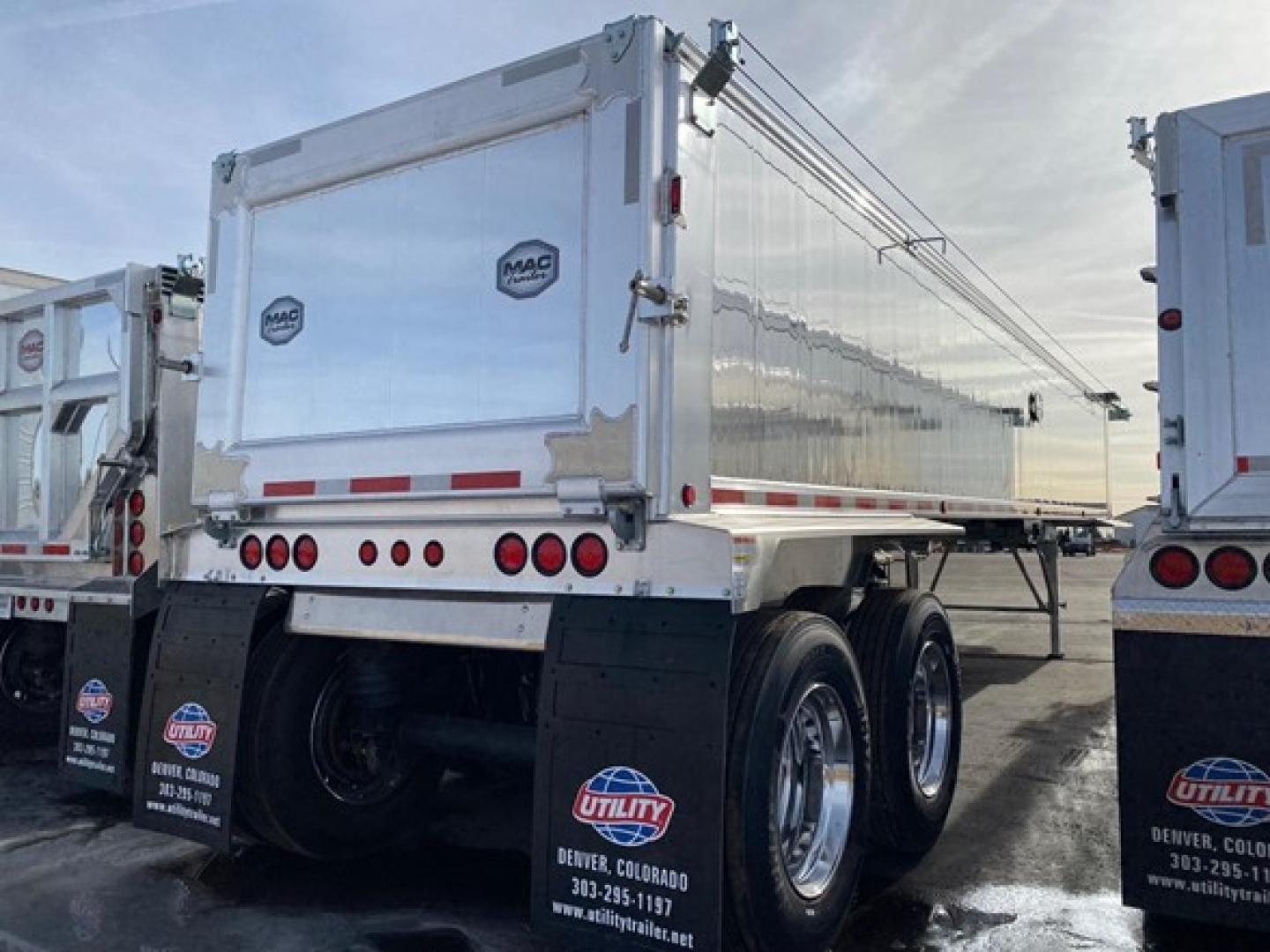 Dump trailer rear view showing MAC brand emblem, dual rear doors, and triple-axle configuration with mudflaps and reflective strips.