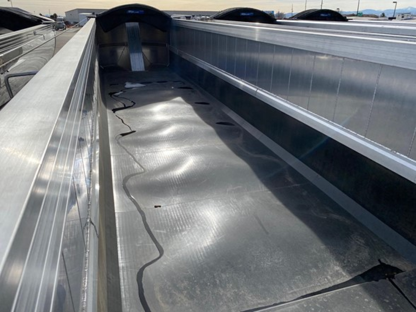 Dump trailer bed showing metal reinforced interior with ribbed side walls and a smooth metal floor.