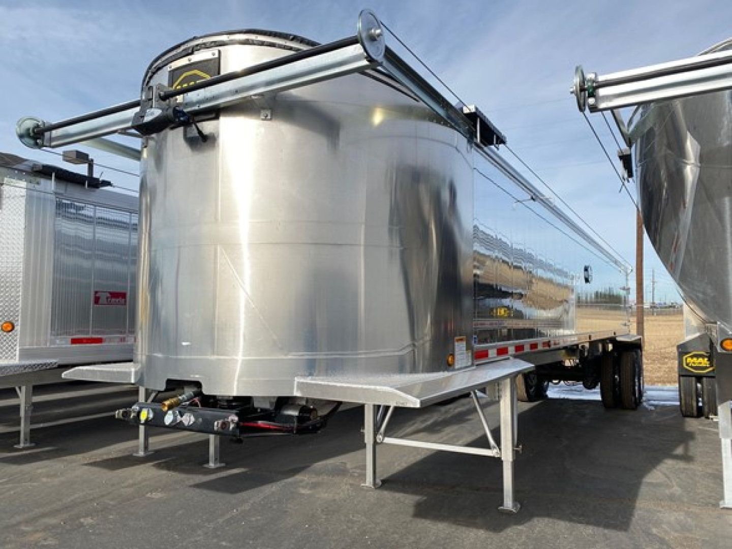 Galvanized steel dump trailer tank with front landing gear and rear hitch, Mac Light Weight trailer in a dealership lot.