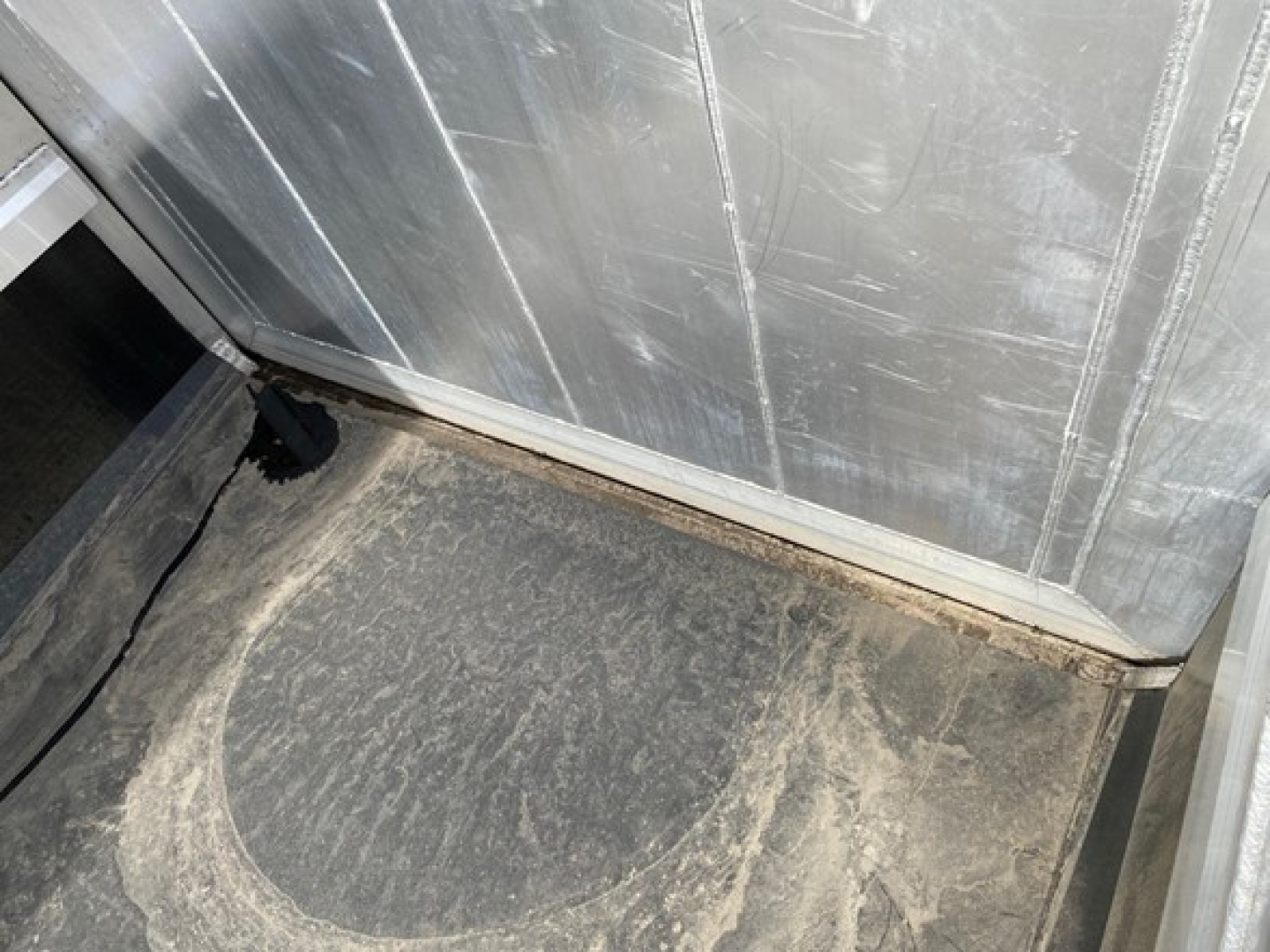 Trailer interior corner showing a dirty floor with wear near the baseboard and metal wall panels.