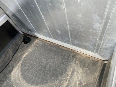 Trailer interior corner showing a dirty floor with wear near the baseboard and metal wall panels.