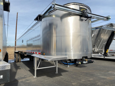 Semi-flatbed trailer with aluminum tank and uncoupled hitch showing support legs and undercarriage, side rails, and polished metal surface