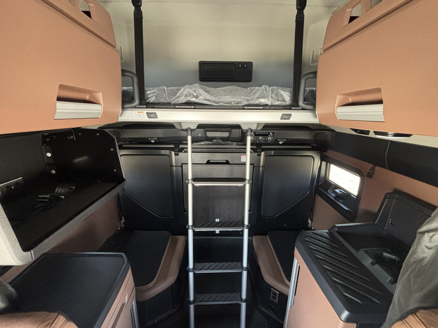 Interior of a new 2027 Mack PR64T76H showing sleeper area with ladder, cabinets, and cockpit in view.