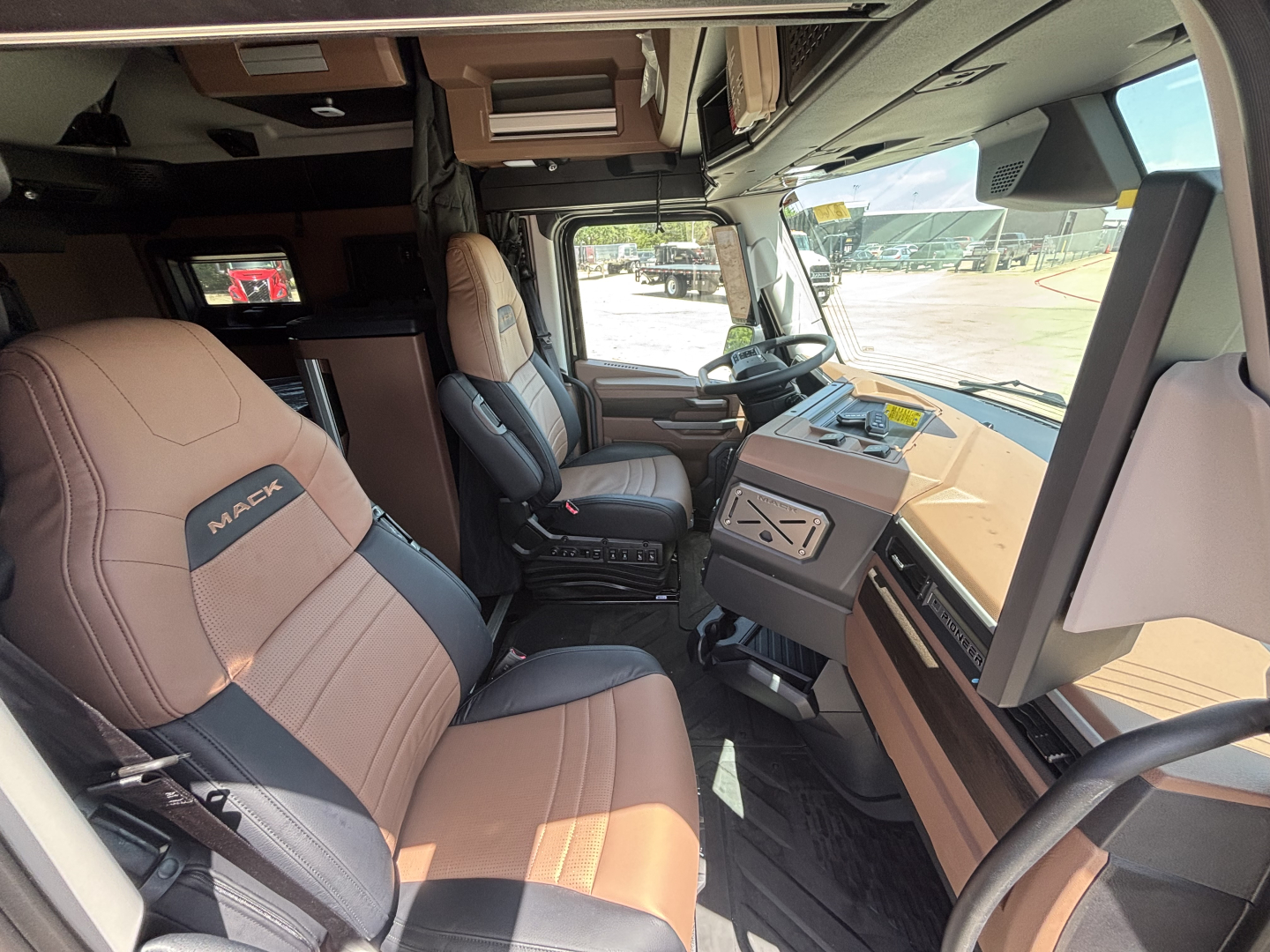 Mack PR64T76H truck cab interior showing tan and black seats, dashboard, steering wheel, and side windows.