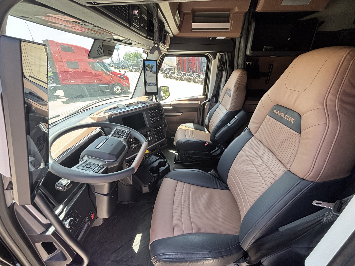 Cab interior of a 2027 Mack PR64T76H showing steering wheel, dash, and two-tone leather seats with Mack logo on the seat.