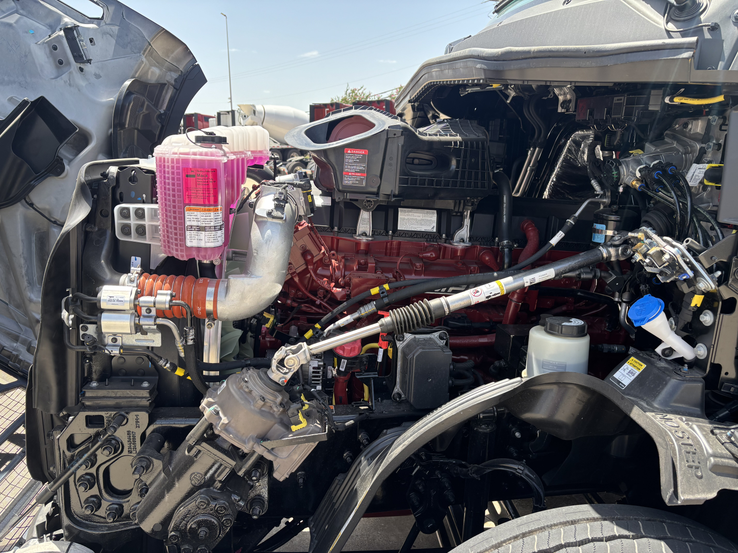 Mack PR64T76H engine bay with red engine block, pink coolant reservoir, and various hoses and components visible.