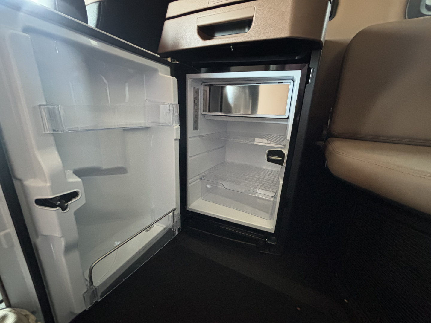 Truck cab interior showing a small refrigerator/freezer unit with door open, located under the center console.