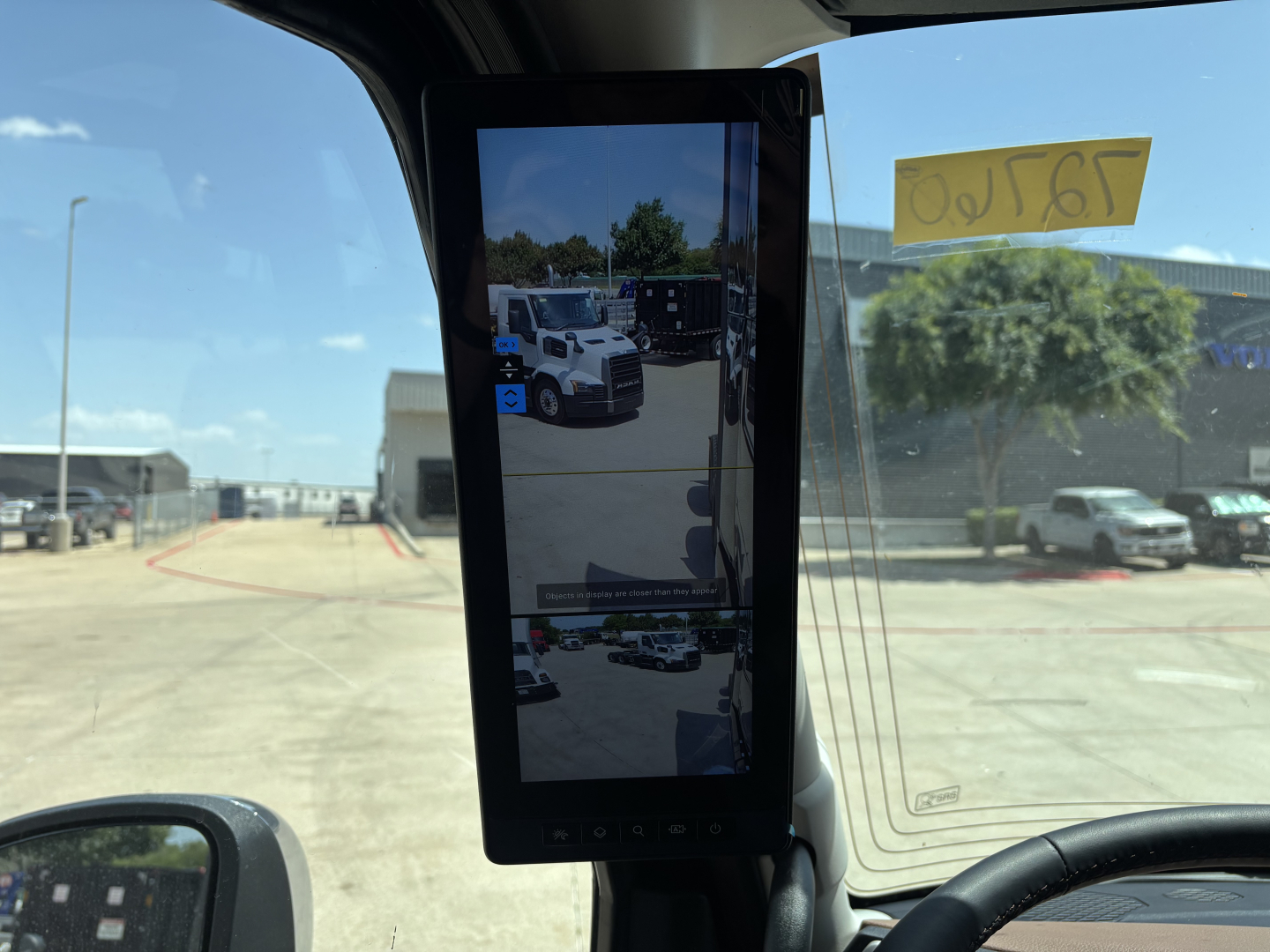 Truck cab interior with a tall vertical tablet display mounted near the windshield showing a reflection of a dealership lot