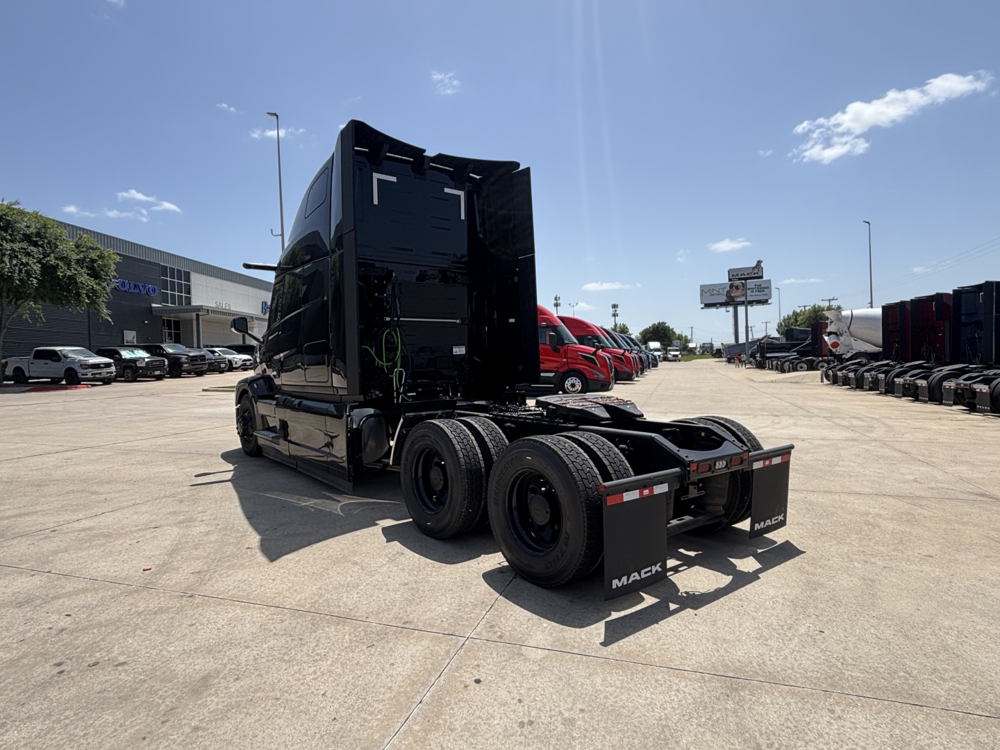 Mack PR64T76H tractor cab and 6x4 axle configuration viewed from rear-left showing chassis, dual rear axles, and flatbed area with black exterior.