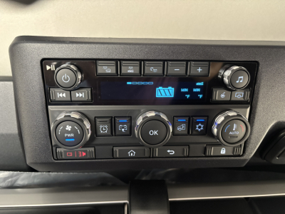 Dashboard controls of a Mack truck cab showing climate and media buttons, central OK button, and digital display panel.