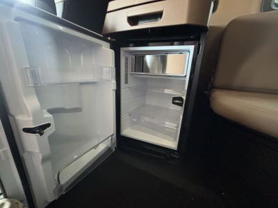 Truck cab interior showing a small refrigerator/freezer unit with door open, located under the center console.