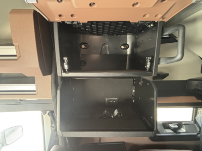 Truck interior center console storage compartments open, showing two rectangular drawers with metal rails and a coiled cable in the lower drawer.