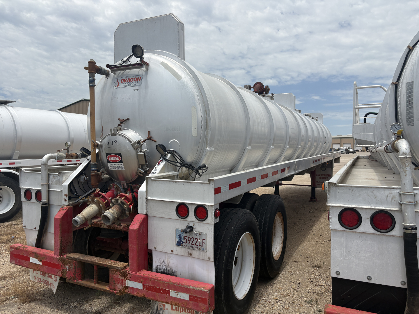 Vacuum trailer tank showing rear manway and hoses, Dragon logo on circular fitting, metal cylindrical tank with rear red bumper and dual rear axles.