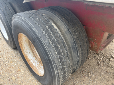 Dual rear wheels of a trailer showing worn tires and rims with rusted hub, red trailer frame in background.