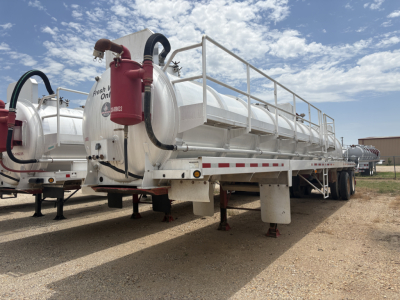 Vacuum trailer with large cylindrical tank and red fire extinguisher mounted at rear, metal railings along top, white exterior, parked on dirt lot.