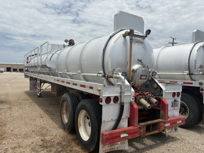 Vacuum trailer with a cylindrical stainless tank mounted on a heavy-duty dual-axle chassis, rear red bumper, piping and valves, and rear safety lights.