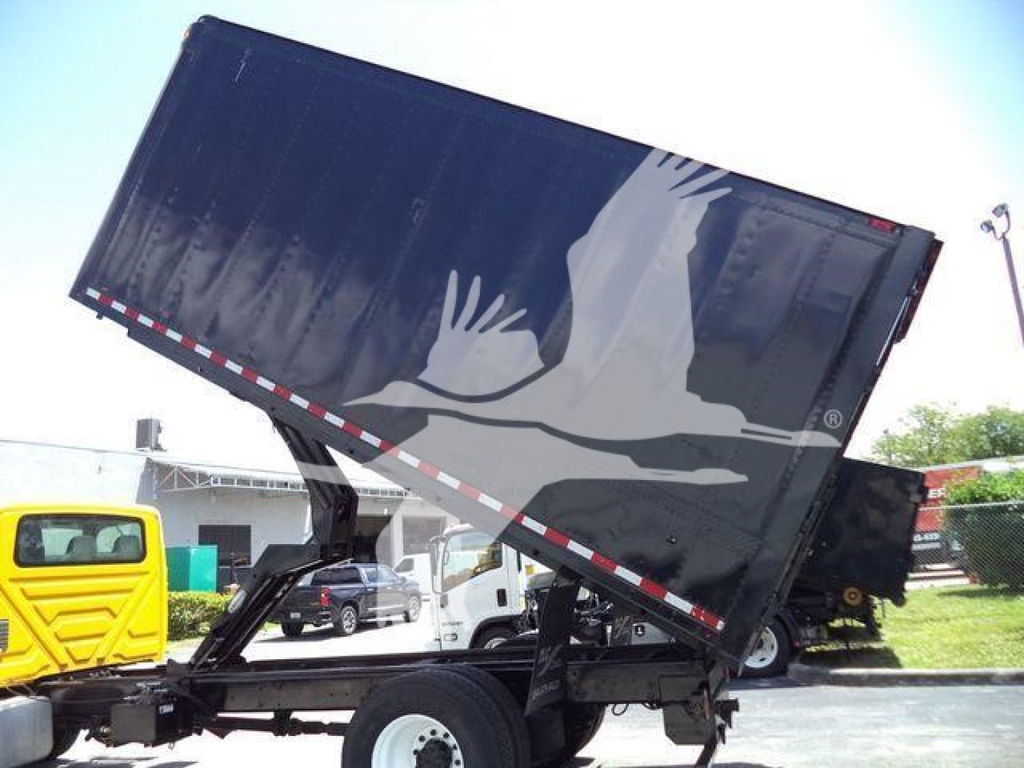 Truck dump bed with hydraulic tilt showing side graphic of a dove and crane truck in background.