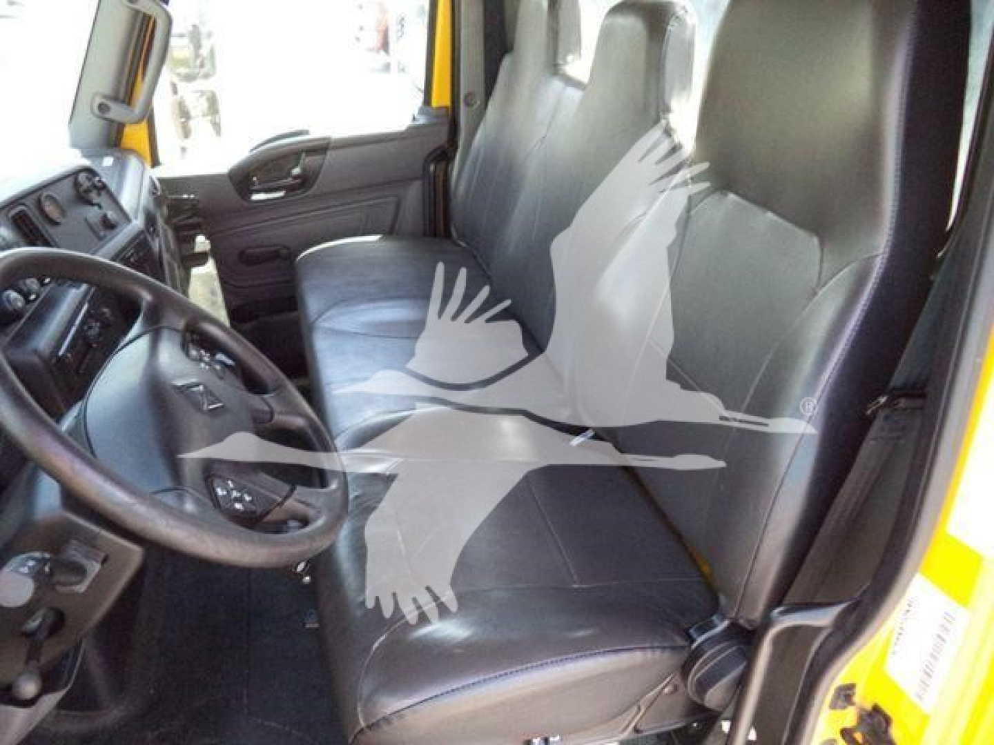 Truck cab interior showing driver's seat and passenger seat with steering wheel and dashboard visible; part of door frame and window; front seat area of a 2020 International MV in a utility/service truck configuration.