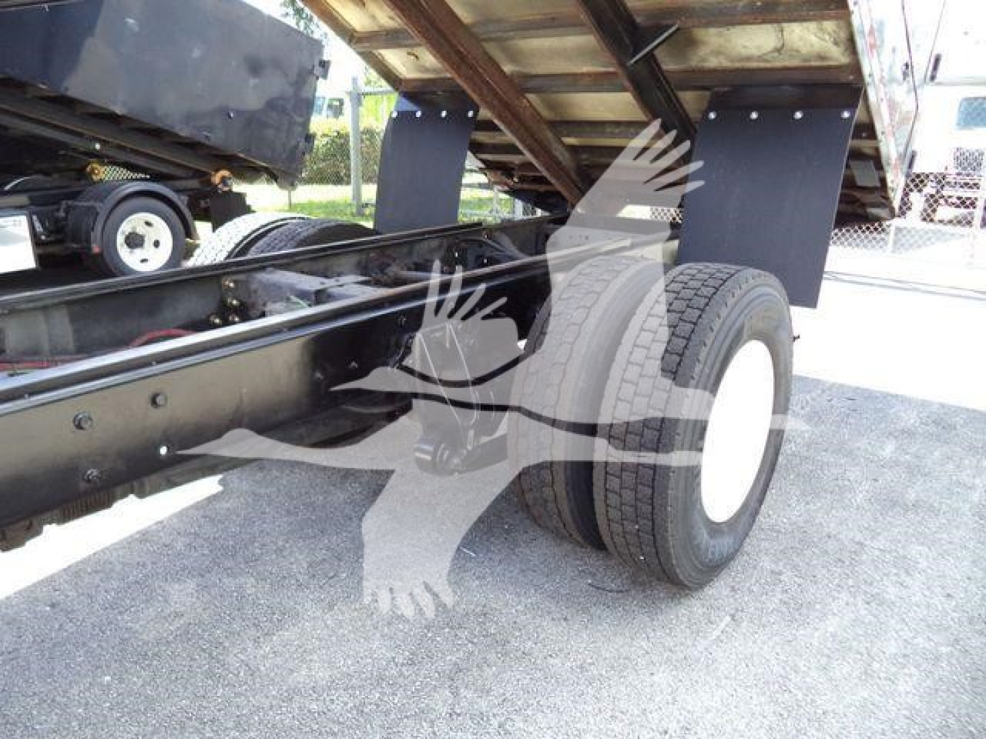 Truck chassis near rear wheels showing dual rear tires and undercarriage with frame, suspension, and hydraulic equipment.