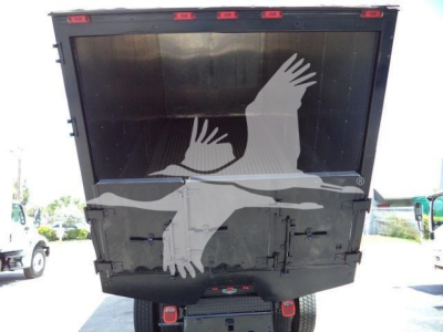 Truck bed or dump body viewed from rear with black painted surface and red taillights; appears to be a chipping or stump grinder wagon. Large white watermark bird graphic overlay across the rear.