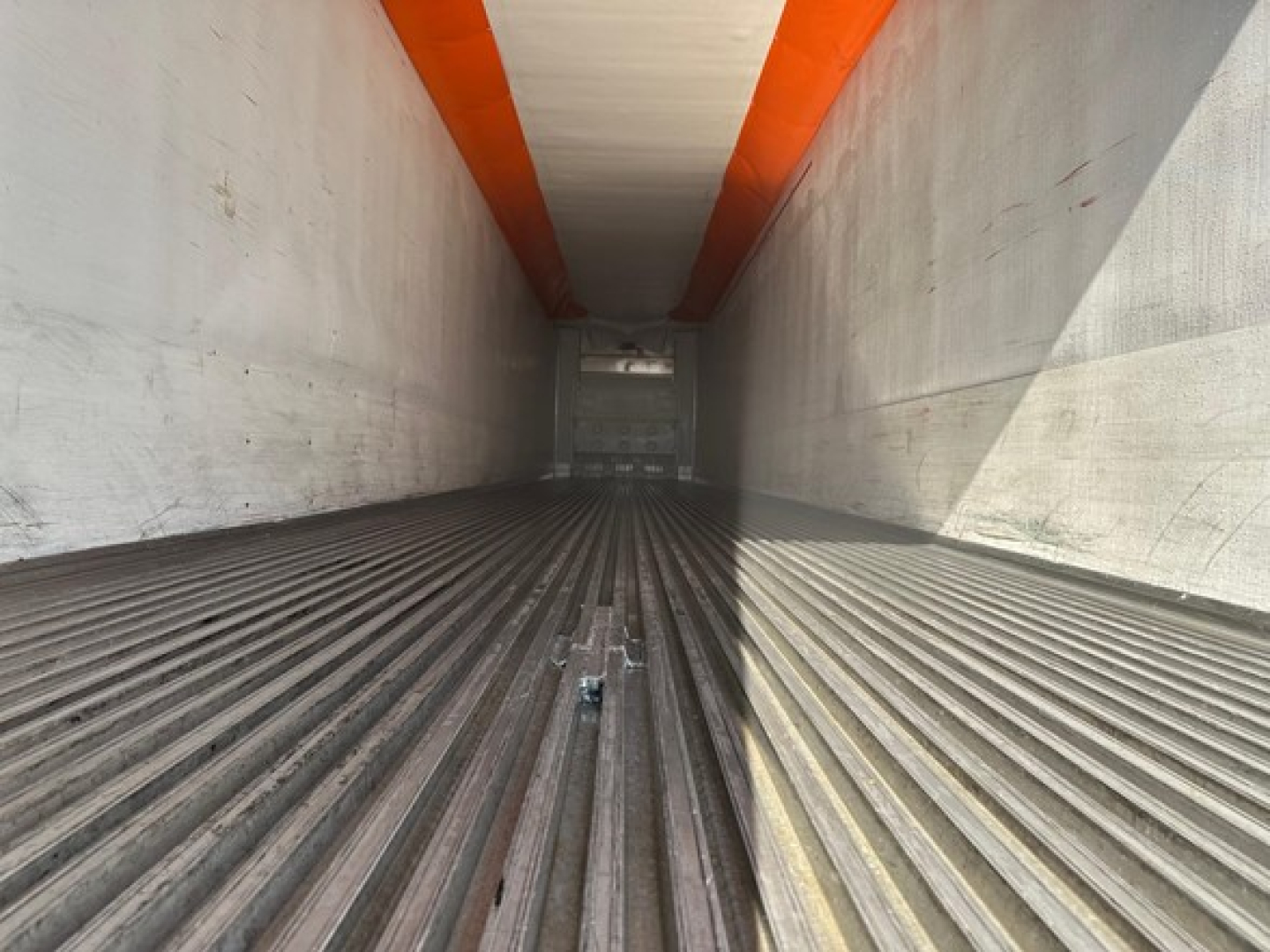 Trailer interior showing ribbed floor with orange ceiling beam and white walls, long narrow cargo area.