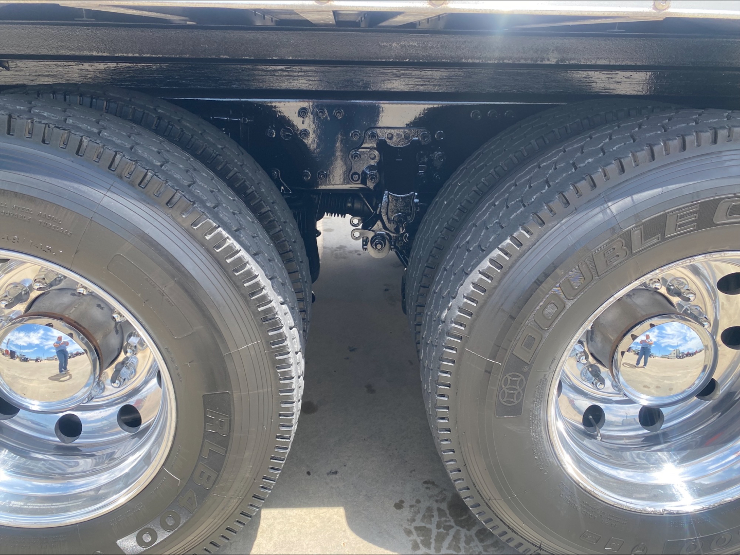 Truck rear axle view showing double wheels and suspension components between tires with chrome hubcaps and tire branding visible.