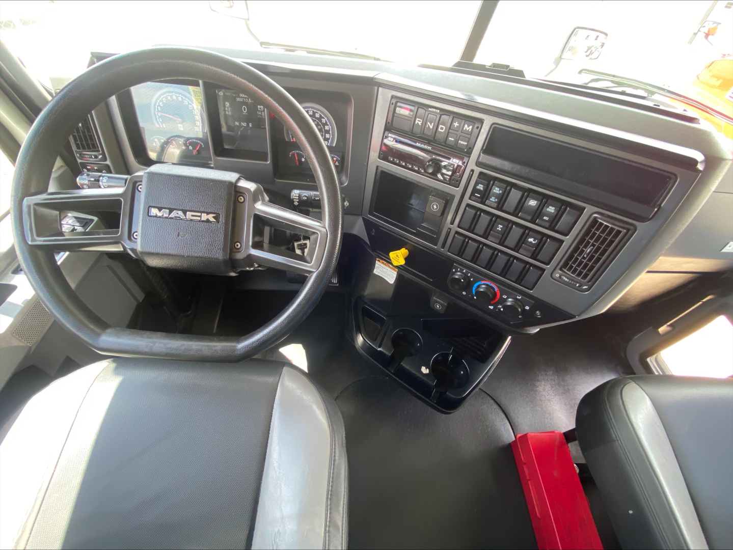 Cab interior of a 2019 Mack AN64 box truck showing steering wheel with MACK badge, dashboard with gauges, central console, and control switches.