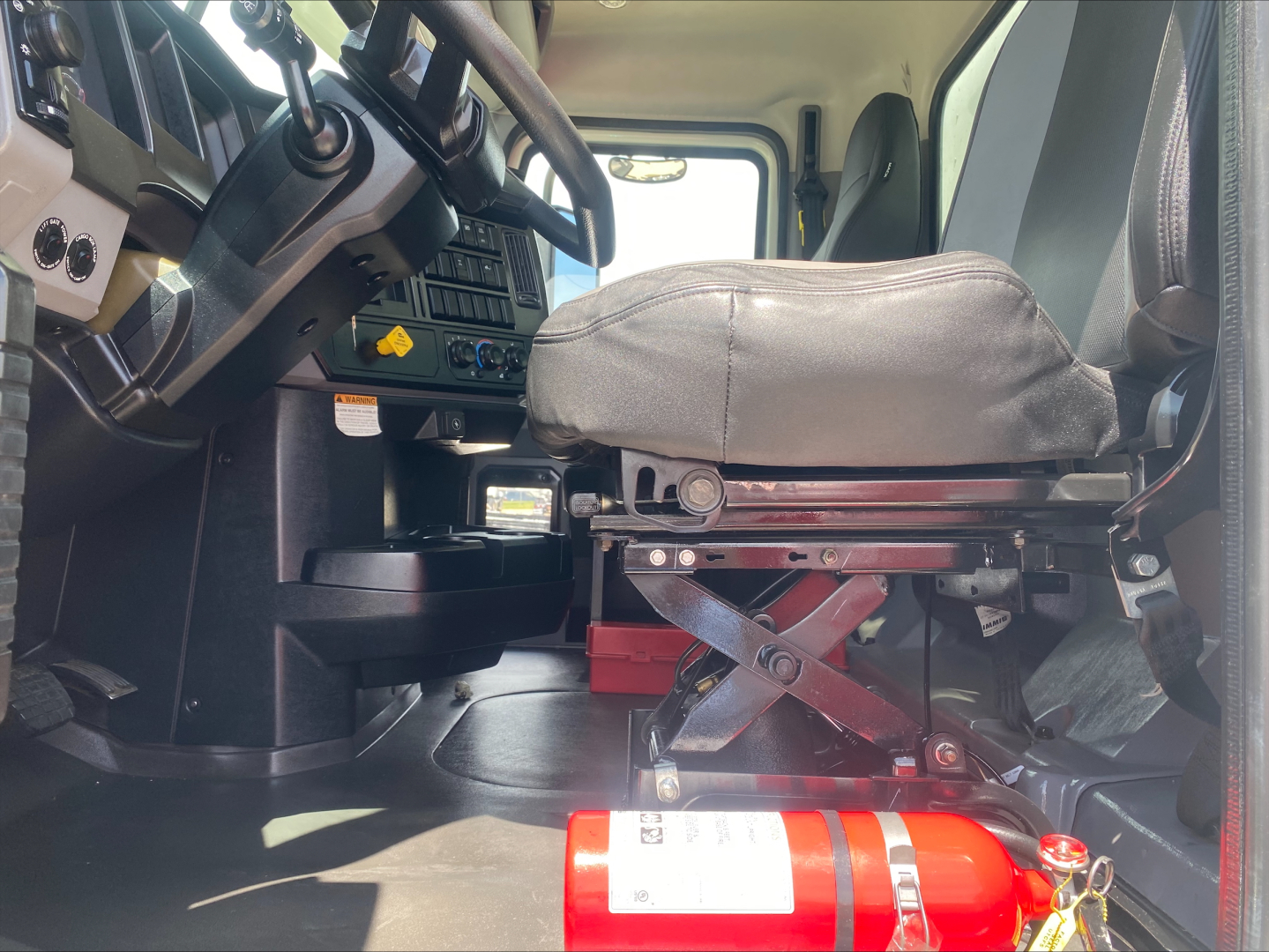 Truck cab interior showing driver's seat and dashboard with fire extinguisher in foreground.
