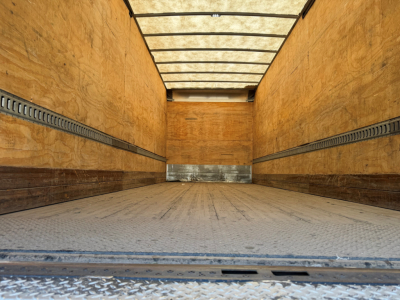 Truck trailer interior showing empty cargo space with wooden sidewalls and metal floor, viewed from back door. 