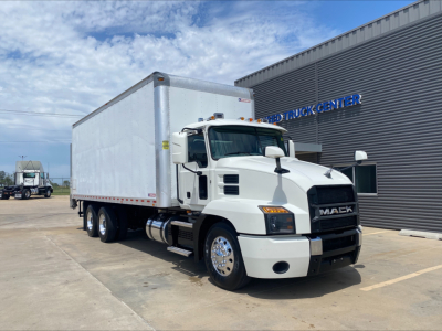 Truck cab in front view showing Mack AN64 box truck with white cab and silver cargo box parked outside a dealership.