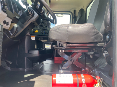Truck cab interior showing driver's seat and dashboard with fire extinguisher in foreground.